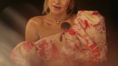 Gece elbisesi giymiş bir kadın aynanın önünde makyajını düzeltir. Karanlık bir odada aynanın önünde güzel bir kız. Video yansıtma.