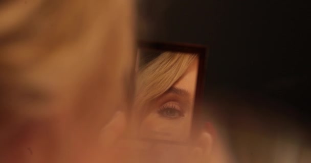 夜のドレスを着た女性は 鏡の前で化粧を修正する 鏡の前にいる少女 暗い部屋で鏡の前で美しい女の子 ミラーリングフレーム — ストック動画