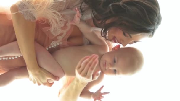 彼女の腕に小さな裸の子供を抱えている美しい母親の垂直ショット 美しい髪型と化粧をした若い母親が腕に赤ん坊を抱えている クローズアップ スローモーション — ストック動画