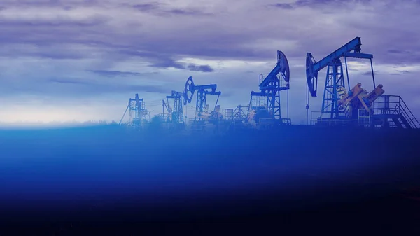 Oil pumps at sunset, industrial oil pumps equipment. Sunset and darkness. Oil field in the fog. Blue toning. Crisis in the oil production industry dramatic concept.