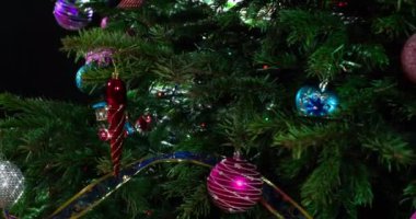 Parlak parlak çelenklerle süslenmiş Noel ağacı dalları ve Noel süslemeleri kameranın önünde yavaşça hareket ediyor