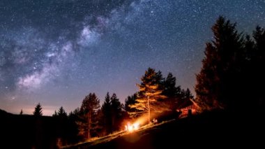 Bunch of friends sitting over campfire in summer nature forest under magic milky way galaxy stars in starry night sky Astronomy Space Time lapse, 4k, Zoom in. 