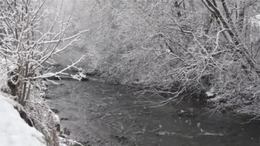 It is snowing in frozen snowy nature with mountain river stream in cold winter background