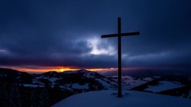 Colorful sunrise in winter mourning over countryside nature with religious christian steel cross in top of snowy hill with fast motion clouds sky Time lapse, Panoramic view