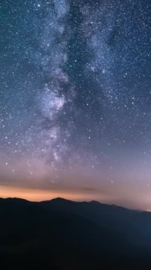 Samanyolu galaksisinin dikey videosu ve hızlı bulutlar yıldızlı gece gökyüzünde dağların ve kırsal trafik manzarasının üzerinde hareket ediyor. Astronomi zamanı hızlandırılmış panorama sosyal medya hikayeleri için ideal.