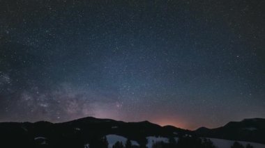 Time lapse video of peaceful winter night in mountains with millions stars with milky way galaxy moving over forest nature. Night to day astronomy timelapse, travel background, 