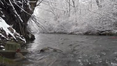 Nehir kış dağlarında akıyor, doğa donmuş karlı ağaçlarla, arka planda..