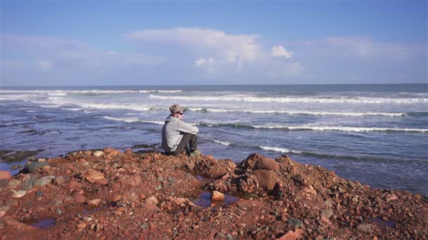 Férfi Kalap Napszemüveg Meditálni Vörös Sziklás Strand Marokkó Óceán Partján — Stock videók