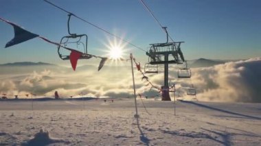 Dağlarda güneşli bir kış sabahı yeni sezonun açılışından itibaren boş bir teleferikle kayak merkezinde. Arka planda güneş yıldızı ve ön planda rüzgarda yavaşça hareket eden küçük bayraklar. 