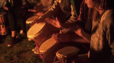 Bir grup arkadaş ateşin başında oturuyor ve sakin bir yaz akşamı doğasında davul çalıyorlar. Djembe 'de davul çalıyorlar..