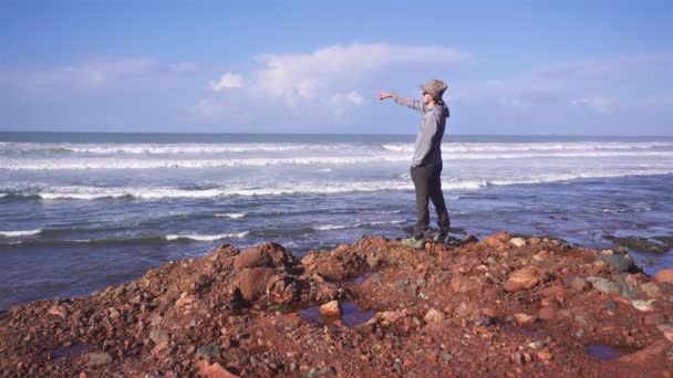 Şapkalı Adam Parmağını Fas Okyanus Kıyısındaki Kumsalda Açık Denize Doğrultuyor — Stok video