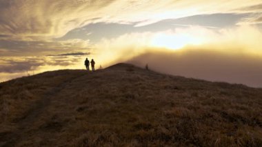 Sonbahar sabahı sisli dağlarda güneşin doğuşunu seyreden turistler. Sisli bulutların üzerindeki altın saat 