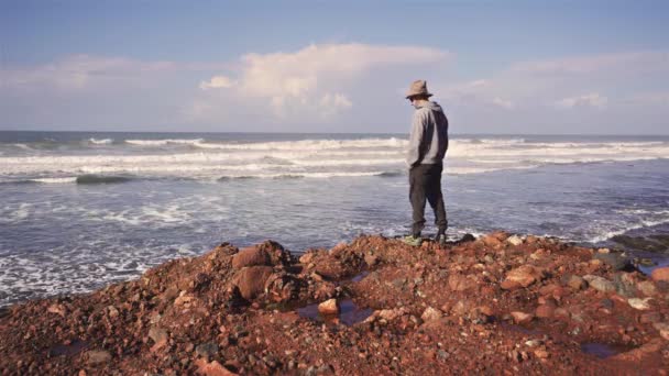 Człowiek Kapeluszu Spaceruje Skalistej Plaży Patrzy Niekończący Się Ocean Spokojną — Wideo stockowe
