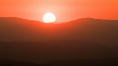 Turuncu günbatımıyla yaz doğasında dağların siluetinin üzerinde renkli bir akşam. Zaman aşımı, kapanış, arkaplan. 