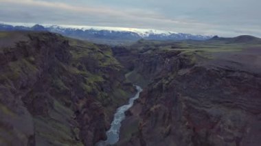 Karanlık volkanik nehir kanyonundan dramatik İzlanda dağları manzarasına doğru uç. Hava görünümü 