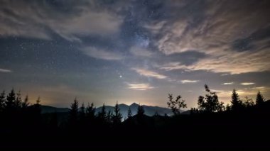 Samanyolu galaksisinin yıldızları ve dağların üzerinde hareket eden bulutlarla dolu güzel bir yaz gecesi manzarası. Zaman aşımı, yakınlaştır. 