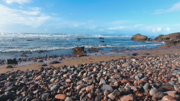 青い空とゆっくりとした動きの波と美しい晴れた日の丸い小石とロッキーな海岸 トラベルモロッコの背景 — ストック動画