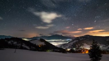 Yıldızlı gece gökyüzünün panoramik manzarası. Yıldızlar ve rengarenk bulutlar. Kış dağları üzerinde hızla ilerleyen karlı doğa manzarası. Astronomi Zaman Hızı, Pan, Takip Et