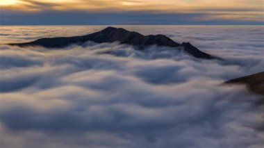 Pofuduk bulutların zaman akışı, altın gün batımında sisli Alp dağlarında hızla hareket ediyor. Huzurlu doğal manzara, uzun pozlama.