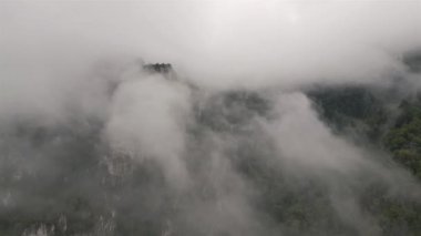 Dünyanın üzerinde, sisli bulutlar dağların arasında sürükleniyor, onları gizem ve güzellikle örtüyor, rahatsız edici derecede güzel bir hava perspektifinden, mistik ve rüya gibi bir hava manzarasından görüldüğü gibi..