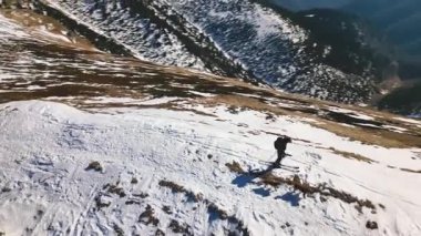 Karlı bir Alp sırtında gezen genç adamın panoramik hava manzarası, köpekleri eşliğinde, Alp dağlarında altın güneş ışığı parlarken ve bahar mevsiminin başlarında ufku gözler önüne sererken