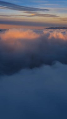 Güneşin ilk ışığı sisli dağlara dokunur, tüylü bulutların üzerine ılık bir parıltı saçar, dinginlik ve merakla dolu sakin dikey bir manzarayla yakalanır.