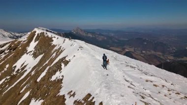İnsanlar ve köpekler baharın başlarında kayaklarla yüksek dağları keşfeder. Yukarıdan çekilen bu sahne, doğanın ve özgürlüğün geniş bakış açısıyla zirvede kalan son karı gösteriyor.