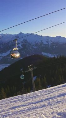 Avusturya 'daki Zell am See Kayak Tesisi' nin karlı yamaçlarının üzerinde bir kayak kaldırma kablecarının dikey videosu. Güneşli bir kış tatili sırasında Alpler 'in manzarası turizm ve seyahat içeriği için mükemmel..