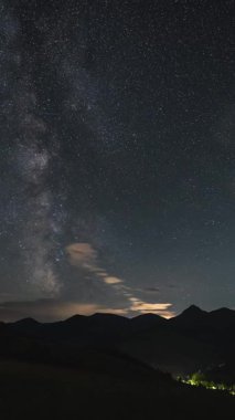 Samanyolu 'nun zamanı ve kara dağların üzerinde sürüklenen bulutlar. Sosyal medya için astronomi, yıldızlara bakma ya da doğal rahatlama için ideal gece gökyüzünün dikey videosu.