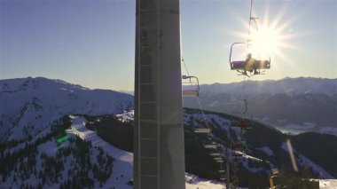 Güneşli bir kış gününde, karlı bir dağ manzarasının üzerinde, bir teleferiğe binen kayakçılar. Göz kamaştırıcı dağ manzarası, kış turizmi, kayak tatili ve tatil macerası için mükemmel..