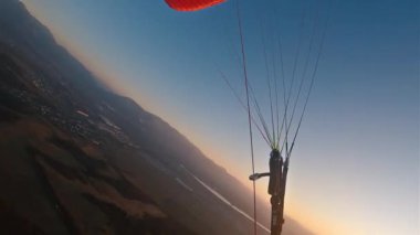 Gün batımındaki yamaç paraşütü macerasından dinamik POV görüntüleri kırmızı paraşüt kanadında sallanan manevralar, parlayan ufuklar ve adrenalin pompalayan hareketler gösteriyor..