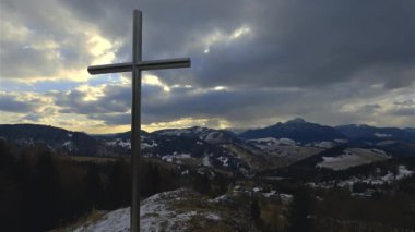 Tepenin üzerinde duran çelik haç büyüleyici dağlık manzaralı bir tepe. Dramatik bulutları olan barışçıl erken bahar atmosferi, manevi, dini ve doğa içeriği için ideal..