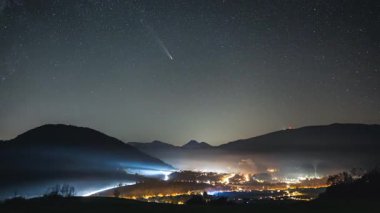 Yıldızlı gece gökyüzünde Tsuchinshan Atlas kuyruklu yıldızı ve Samanyolu galaksisi yıldızlarıyla trafik tarafından aydınlatılmış sisli bir kırsal bölgede güzel bir zaman atlaması. Astronomi ve uzay keşfi görüntüleri 4K.