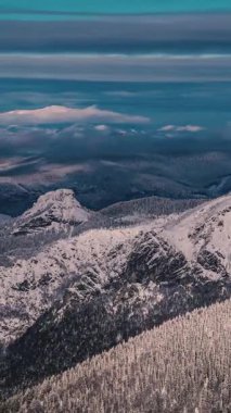 Dikey zaman atlamalı panorama donmuş dağların üzerinde hızlı hareket eden bulutları gösteriyor. Karla kaplı zirveler ve dinamik gökyüzü, kış doğası için ideal doğa, yürüyüş, turizm, dağcılık, açık hava macerası