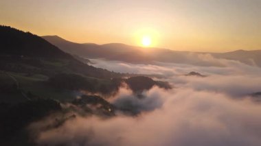 Vadi boyunca sürüklenen sisli bulutlarla birlikte Altın Gün Doğumu 'nun hava manzarası. Güneşin doğal ışığıyla sakin doğal manzara, seyahat, belgeseller, arka planlar veya rahatlama için ideal