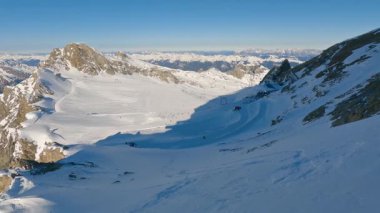 Kitzsteinhorn tepesinden görünen karlı Kaprun buzullu kayak merkezinin nefes kesici panoramik manzarası. Açık mavi gökyüzü, dağlık dağlar ve Alpler 'de güneşli bir tatilde kış sporları aktiviteleri.. 