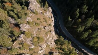 İnsansız hava aracı görüntüleri yoğun orman ve dolambaçlı yollarla kayalık dağ manzarasına doğru uçuyor. Manzaralı kuş bakışı seyahat, keşif, doğa veya belgesel içeriği için mükemmel. 