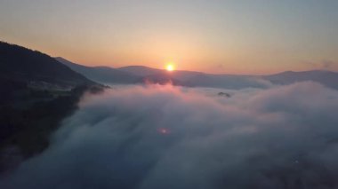 Güneş doğarken sisli bir orman manzarasının havadan görüntüsü. Altın ışık sislerle kaplı dağların üzerinde parlıyor, saf doğada gizemli ve huzurlu bir sabah atmosferi yaratıyor.. 