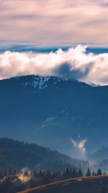 Sis ve ağaçlarla kaplı sonbahar dağlarının üzerinden hızla geçen dikey bulutlar. Mevsimsel atmosfer ve altın ışıkla dramatik doğa hareketini yakalar. Sosyal medya içeriği için ideal. 