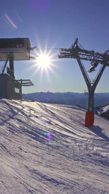 Zell am 'da karla kaplı yamaçlar mavi gökyüzü, parlak güneş ve kış tatili atmosferiyle kayak merkezine bakın. Sandalye kaldırma, dağlık arazinin üzerinde yolculuk için ideal bir dikey video ile hareket eder.