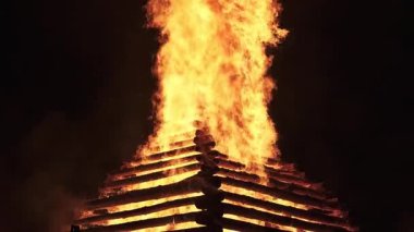 Karanlıkta yanan büyük bir şenlik ateşinin yavaş çekim görüntüleri. Uzun alevler, yoğun, atmosferik ve ateşli bir sahne yaratarak, gece karanlığında dramatik bir şekilde yükselir. Ritüeller, festivaller veya etkinlikler için mükemmeldir.