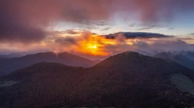 Turuncu ve morumsu ormanlık tepelerde şafak sökerken rüzgarlar bulutları hızla gökyüzüne doğru sürüklüyor. Renkli bir dağ gündoğumunun pürüzsüz hızlandırılması. Doğa ve seyahat görüntüleri için ideal..