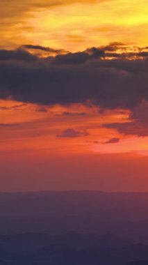Dağ siluetlerinin üzerinde altın ve turuncu bulutlar olan günbatımı gökyüzü dikey zaman atlaması manzarası. Sakin, huzurlu bir gün. Güzel, sıcak renkler, mükemmel bir arka plan.. 