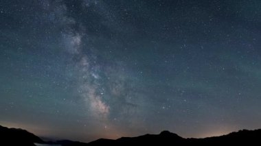 Destansı bir zaman atlaması, Samanyolu galaksisinin açık yıldızlı gece gökyüzünde dağ siluetleri üzerinde yükseldiğini gösteriyor. Milyonlarca yıldız ilk ışıktan önce büyülü bir gece manzarası yaratır.. 