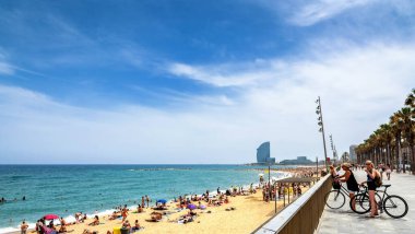 Barcelona, Spain - July 6, 2017:  day view of tourists walking by Passeig Maritim in front of Barceloneta beach and Mediterranean, sea with W hotel in the background, in Barcelona, Spain.