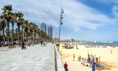 Barcelona, Spain - July 6, 2017: day view of tourists walking by Passeig Maritim in front of Barceloneta beach and skyscrapers in Barcelona, Spain.