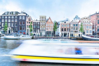 Amsterdam, Netherlands - June 12, 2019: long exposure day view with typical Dutch houses, canal and shops  in Amstel, Amsterdam, Netherlands. clipart