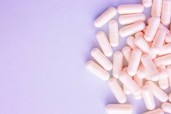 stock image Pink capsules with medicine on a purple background. Handful of pills, treatment concept. Copy space.