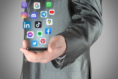 Uçan sosyal medya uygulamalarının simgelerini içeren akıllı bir telefon taşıyan iş adamı, gri arka planda, akıllı telefon kavramında sosyal medya