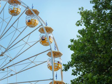 Mavi gökyüzüne ve yeşil ağaca karşı sarı dönme dolap. İnsanlar için eğlence, eğlence parkı.